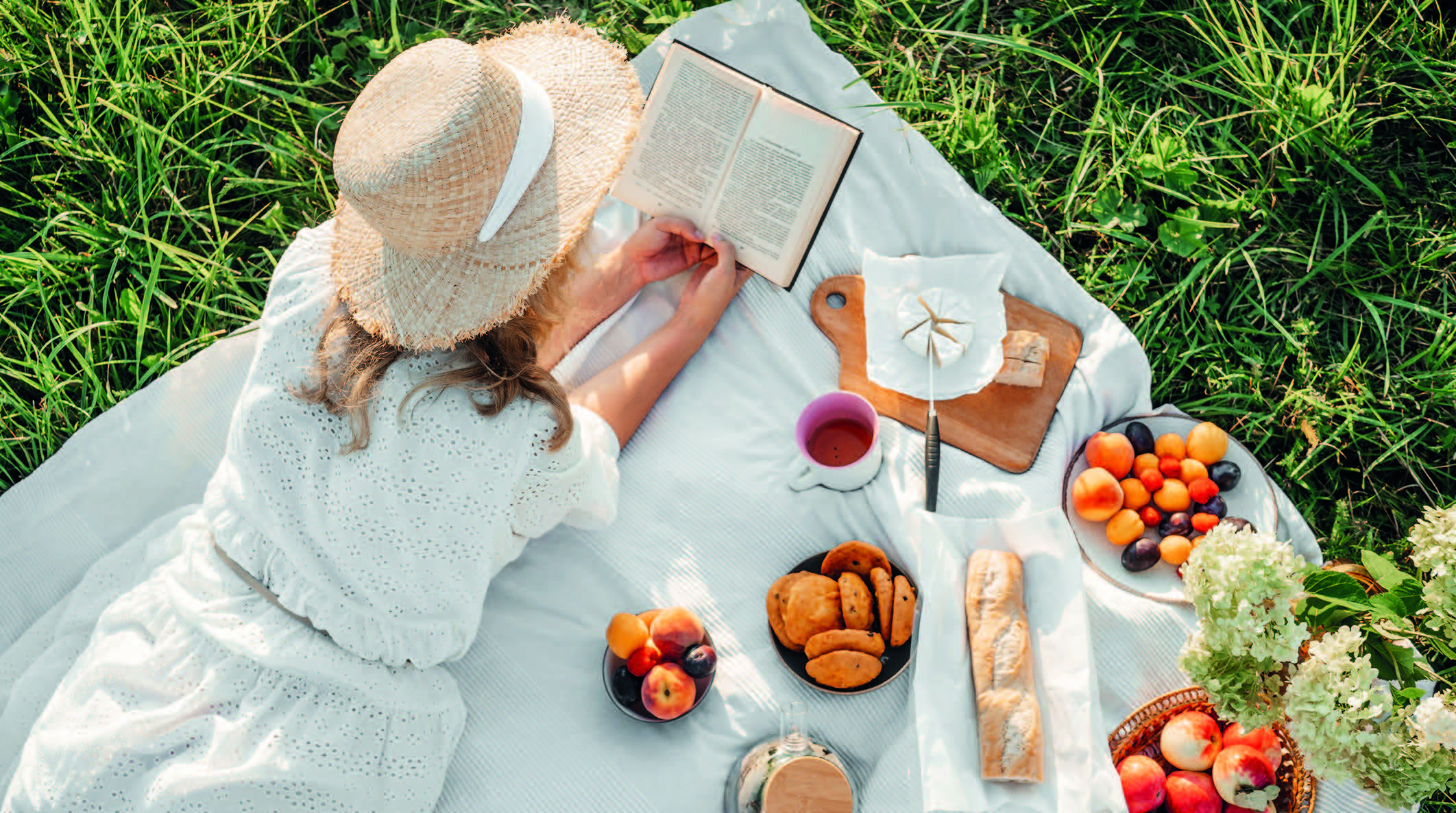 Femme allongée sur un plaid lors d'un pique-nique, lecture au soleil, ambiance printemps été.