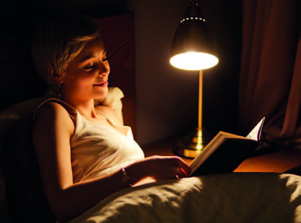 Femme lisant au lit sous une lumière douce avant de dormir.