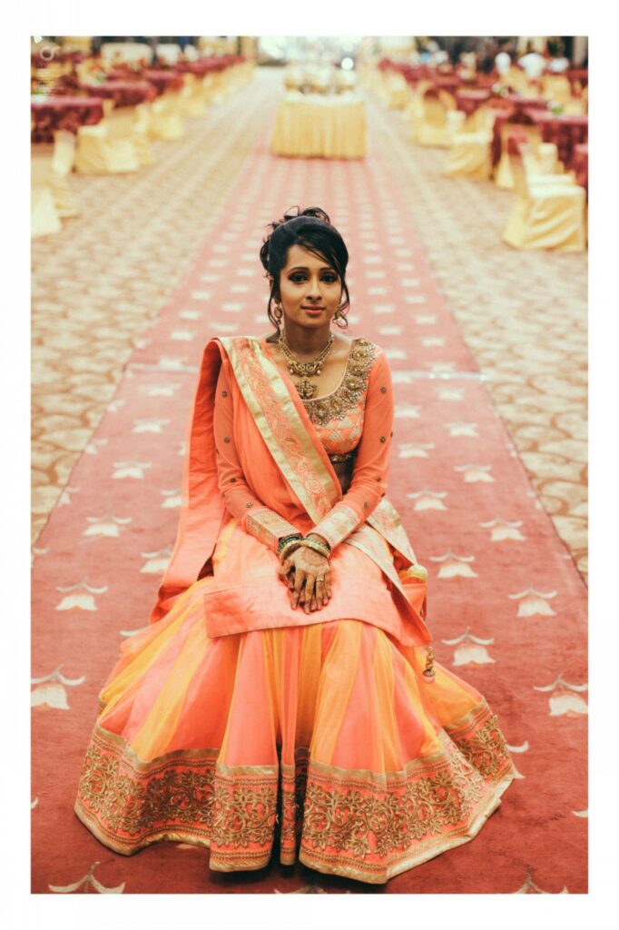 Arpitha Savale assise, vêtue d’une tenue de cérémonie orange et de bijoux dorés.
