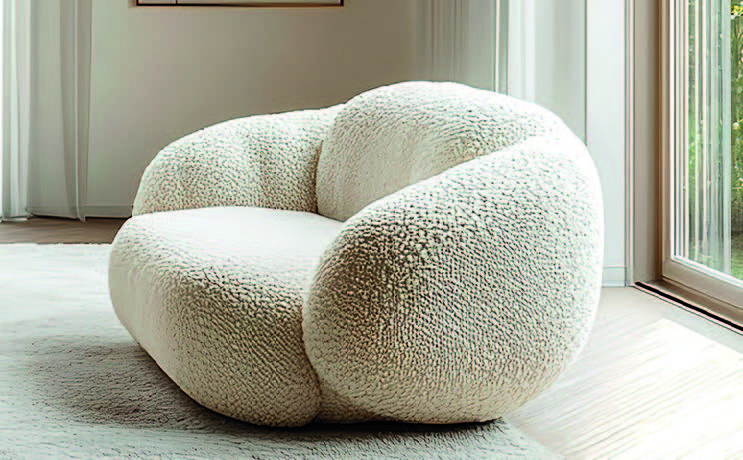 Fauteuil blanc aux volumes arrondis et au revêtement texturé, placé près d’une fenêtre.