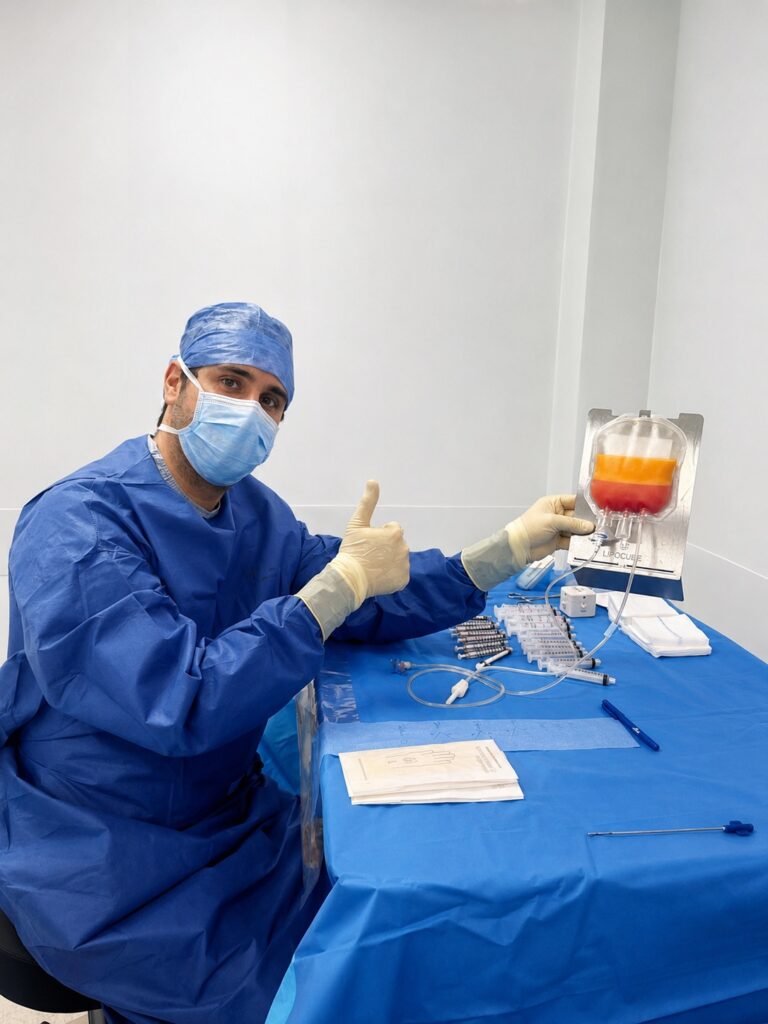 Le Dr Édouard Mas en tenue médicale bleue, près d’une table d’instruments et d’un dispositif contenant un liquide en plusieurs couches.