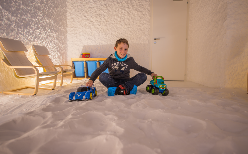 Enfant assis dans le sel avec des véhicules jouets, dans une salle équipée de fauteuils.
