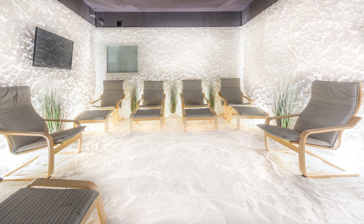 Chambre de sel avec plusieurs fauteuils de relaxation, des murs blancs texturés et un sol recouvert de sel.