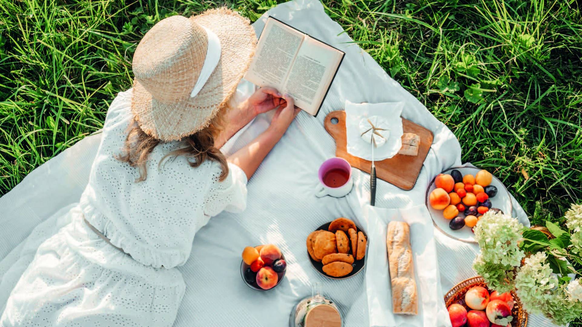 Femme allongée sur un plaid lors d'un pique-nique, lecture au soleil, ambiance printemps été.